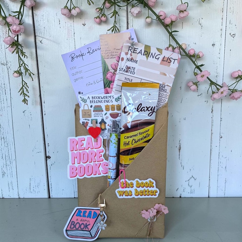 May include: A brown paper envelope containing a book review sheet, a reading list, a Galaxy caramel hot chocolate packet, a patterned pen, and stickers reading Read More Books, The Book Was Better, and Read A Damn Book with a heart clip.