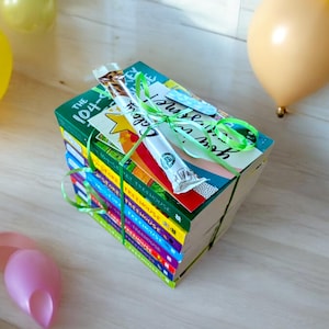 Könnte beinhalten: Ein Stapel bunter Bücher, umwickelt mit grünem Band und einer Karte mit der Aufschrift "Nur für dich!" Die Bücher tragen die Titel "The 104-Story Treehouse" und "The Treehouse" mit unterschiedlichen Nummern.