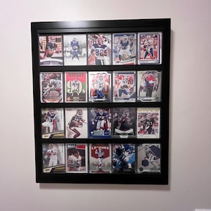 May include: A black framed display case filled with football trading cards. The cards feature various players in action, with team logos and player names visible. The cards are arranged in rows and columns.
