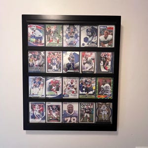 May include: A black framed display case filled with football trading cards. The cards feature various players in action, with team logos and player names visible. The cards are arranged in rows and columns.