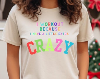 Peut inclure: Un t-shirt beige avec un graphisme coloré qui dit "Je m'entraîne parce que j'ai un peu de folie en plus".