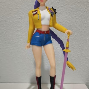 Könnte beinhalten: Figur einer Frau mit lila Haaren, die eine gelbe Jacke, blaue Shorts und schwarze Stiefel trägt und ein Schwert hält. Die Figur steht auf einer schwarzen Basis mit weißem Design. Das Schwert ist rosa und gold.
