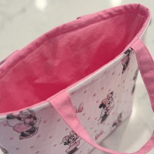 May include: Pink tote bag with a Minnie Mouse pattern and pink handles. The bag features a pink interior and a white exterior with pink polka dots and Minnie Mouse illustrations.
