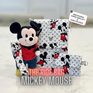 May include: A Mickey Mouse themed set featuring a plush toy, a card wallet, and an ear holder. The items are decorated with a repeating Mickey Mouse pattern on a gray background. The text "THE RIDE BAG MICKEY MOUSE" is displayed.