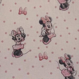 May include: A repeating pattern featuring Minnie Mouse in various poses, wearing a pink dress and bow. The background is a light pink with evenly spaced pink polka dots. The overall design is whimsical and playful.