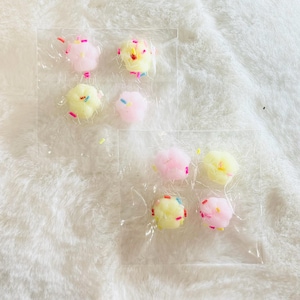 May include: Six small, round, colorful, cotton candy-like decorations in a clear plastic package. The decorations are pink and yellow with colorful sprinkles.