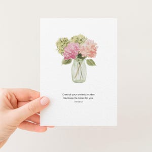 Puede incluir: Una tarjeta blanca con una ilustración de acuarela de un ramo de hortensias rosas y verdes en un jarrón de vidrio transparente. La tarjeta incluye el texto "Cast all your anxiety on Him because He cares for you. 1 PETER 5:7."