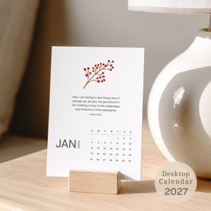 May include: A white desktop calendar card for January 2026, held in a light wood block stand. The card features a red berry branch illustration, the text "See, I am doing a new thing!" from Isaiah 43:19, and a monthly grid for January 2026.