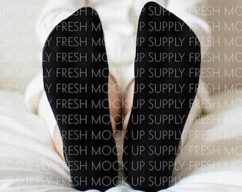 May include: A pair of black socks with the toes and heels turned up, resting on a white bed sheet.