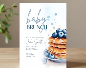 May include: Baby brunch invitation with watercolor design. The invitation features the words "baby brunch" in a soft blue script. A stack of pancakes topped with blueberries is on the right. The invitation includes the name Julia Smith and event details.