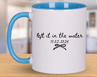 Peut inclure: Mug en céramique blanche avec intérieur et anse bleus. Le mug porte l'inscription "left it in the water" avec la date 11.02.2025 et un motif de nœud en noir.