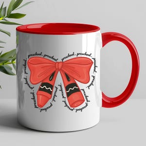 Könnte beinhalten: Weißer Keramikbecher mit rotem Innenraum und Griff. Der Becher zeigt ein rotes Schleifen- und Buntstift-Design mit dem Wort "preschool" in einem kreisförmigen Muster. Ein lustiger und farbenfroher Becher für Vorschüler oder Lehrer.