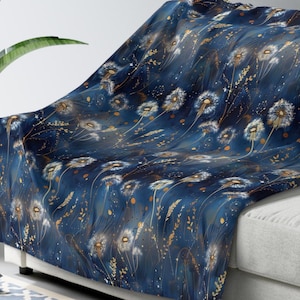 May include: A soft throw blanket featuring a deep navy blue background with a repeating pattern of white dandelion seed heads and delicate gold-coloured botanical sprigs and scattered dots across the entire surface of the fabric.