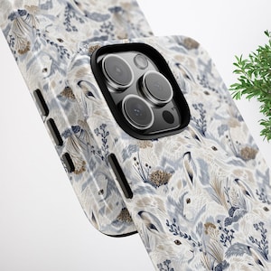 May include: A smartphone case featuring a repeating pattern of white rabbits nestled among blue and tan botanical elements. The case has a black camera module cutout and black side buttons, showcasing a detailed illustration of wildlife.