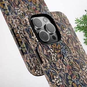 May include: A smartphone case featuring a detailed pattern of brown rabbits nestled among dark blue foliage, green clover, and small white flowers. The case has a black camera cutout frame and black side buttons, showcasing a triple-lens camera system.