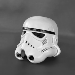 May include: A white plastic Stormtrooper helmet with a black stripe across the top. The helmet has a detailed design with black accents and a visor.