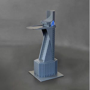 May include: A gray 3D printed model of a skyscraper with a helipad on top. The building has a distinctive angled design and a small "A" printed on the side.