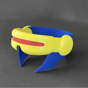 May include: A yellow and blue plastic headband with a red visor. The headband is designed to look like a futuristic helmet.