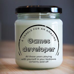 May include: A white candle in a glass jar with a black lid. The label reads "A candle for an amazing Games developer. All those years playing with yourself in your bedroom certainly paid off."