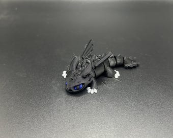 Puede incluir: Figurita de dragón negro con ojos azules y garras blancas. El dragón está en posición de arrastre con las alas extendidas.