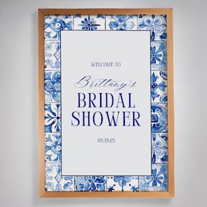 May include: A white sign with a blue and white tile border. The sign says "Welcome to Brittany's Bridal Shower 05.19.25".