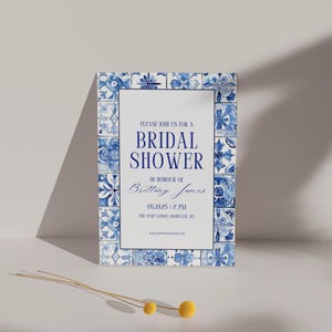 Minimalist bridal shower invitation bordered with blue tiles, propped up on a neutral backdrop with playful yellow billy ball flowers.