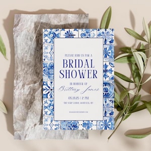 Stylish bridal shower invitation with blue tile design, placed on crumpled paper with olive branches, walnuts, and a candle for a rustic aesthetic.