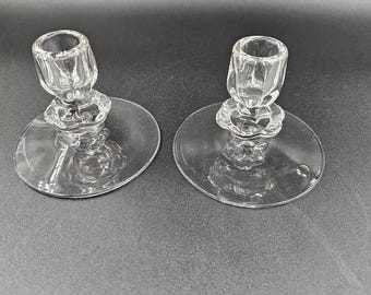 May include: Two clear glass candle holders with a fluted design. Each holder has a round base and a small, round cup for holding a candle.