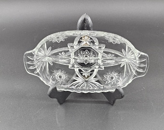 May include: A clear glass divided dish with a starburst pattern. The dish has two sections and is perfect for serving snacks or appetizers.