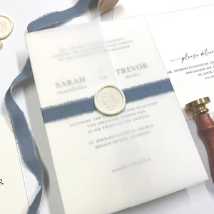 May include: A wedding invitation with a white background and blue ribbon. The invitation features the names "Sarah" and "Trevor" and the date "Saturday, the Second of January Two Thousand Twenty-Two".
