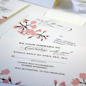 K&ouml;nnte beinhalten: Eine wei&szlig;e RSVP-Karte mit rosa Kirschbl&uuml;ten-Illustrationen. Der Text lautet "We look forward to celebrating with you!" und "Kindly reply by April 3rd, 2015".