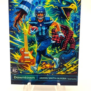 May include: A vibrant trading card featuring a football player in a blue uniform, running with the ball. The card has a colorful, stylized background with an eagle, guitar, and cityscape. Text on the card reads "Downtown" and "Jaxon Smith-Njigba Seahawks."