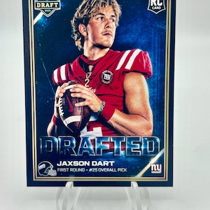 May include: A football trading card featuring Jaxon Dart, drafted in 2025. The card has a blue and gold border, with the text "DRAFTED" prominently displayed. Dart is wearing a red jersey and holding a football.