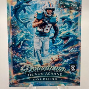 May include: A football trading card featuring a Miami Dolphins player running with the ball. The card has a vibrant, artistic design with dolphins, palm trees, and a "Downtown" sign. The player's jersey number is 28.