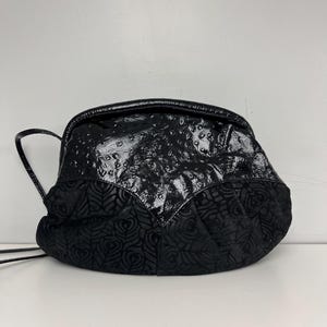May include: A black handbag with a unique design. The top section has a glossy, textured finish, while the lower part features a patterned, velvety fabric. The bag has a rounded shape and a thin strap.