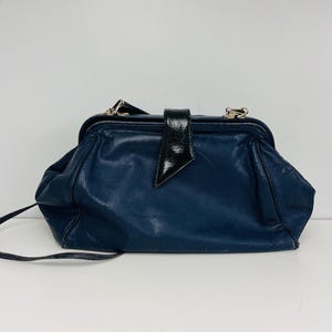 May include: A vintage navy blue leather handbag with a black patent leather clasp. The bag has a rounded shape and a long, thin strap. Silver-toned hardware accents the top of the bag.