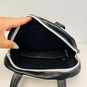 May include: Black and white handbag with a zippered top and two handles. The bag has white stitching and a white trim. The interior is black.
