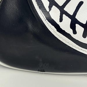 May include: Close-up of a black and white baseball glove. The glove features a black leather exterior with a white accent and a white circular design with black stitching.