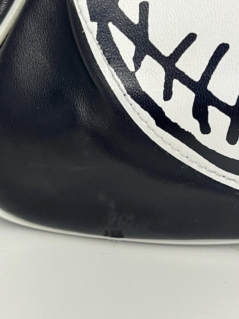 May include: Close-up of a black and white baseball glove. The glove features a black leather exterior with a white accent and a white circular design with black stitching.