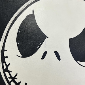 May include: Close-up of a black and white graphic design featuring a character's face. The face is white with black eyes and a stitched-like mouth. The background is black.