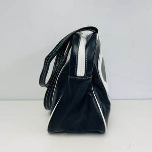 May include: Black and white handbag with a rectangular shape. The bag has a white zipper and white stitching. The handles are black with white stitching. The bag has a white trim.