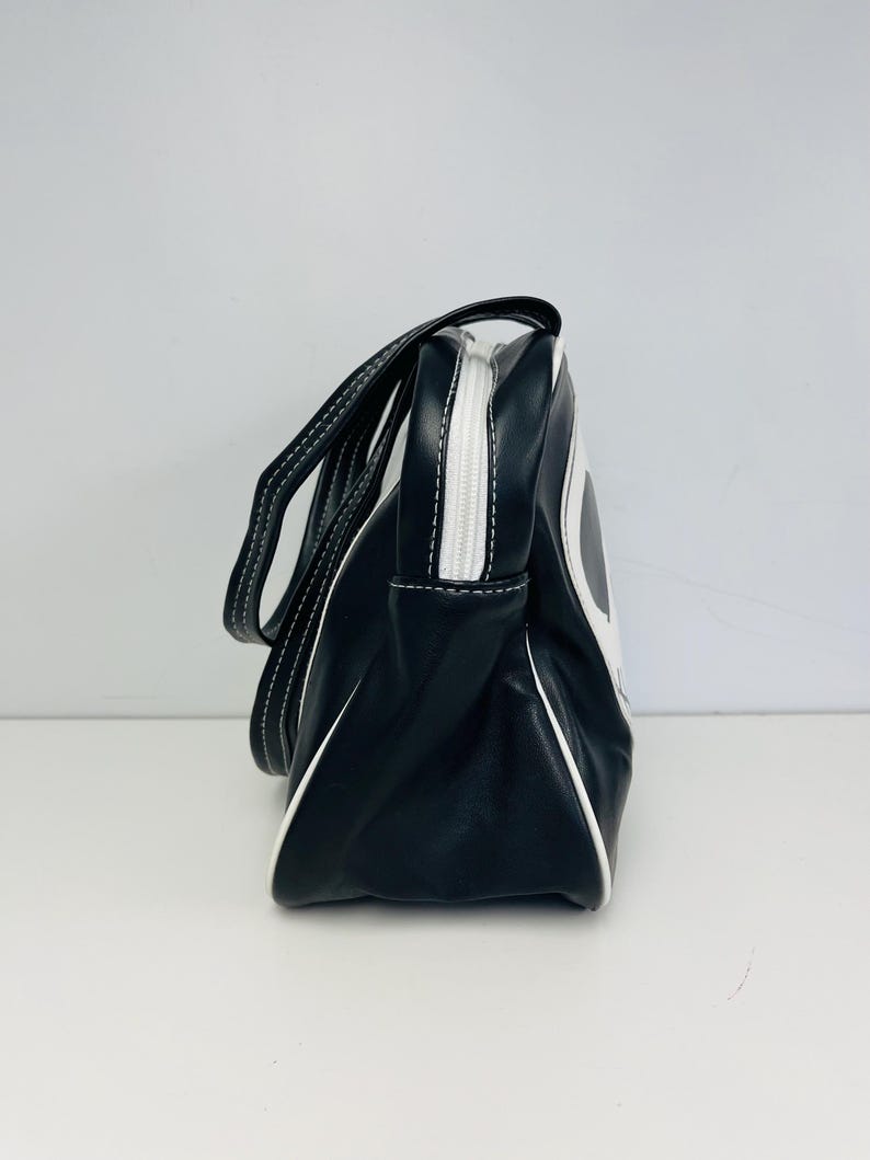May include: Black and white handbag with a rectangular shape. The bag has a white zipper and white stitching. The handles are black with white stitching. The bag has a white trim.
