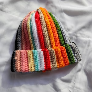May include: A colorful crocheted beanie hat with stripes of black, pink, beige, turquoise, white, red, orange, and green.