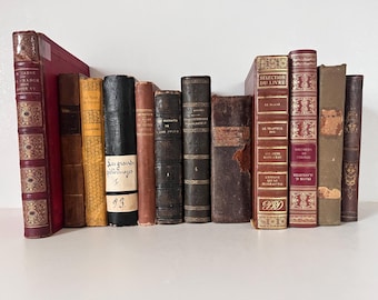 May include: A collection of antique books with various colors and textures. The spines display titles and decorative elements, including gold lettering and embossed patterns. Some books have visible text, such as "Les grands pelerinages" and "SELECTION DU LIVRE".