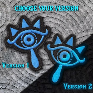 May include: Two embroidered patches featuring a blue eye design with a crown. The patches are outlined in black and have a blue glow effect. The text "CHOOSE YOUR VERSION" and "Version 1" and "Version 2" are displayed.