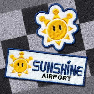 Könnte beinhalten: Zwei gestickte Aufnäher mit einem Sonnenschein-Thema. Einer ist eine Sonne mit Krone, der andere ein Rechteck mit dem Text "SUNSHINE AIRPORT". Beide haben einen weißen Hintergrund mit blauen und gelben Akzenten.