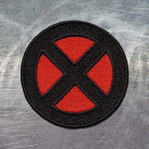 Puede incluir: Un parche bordado circular con un borde negro y una forma de cruz negra centrada sobre un fondo rojo. El diseño consta de cuatro segmentos triangulares rojos separados por una cruz negra gruesa, todo encerrado dentro de un marco circular negro.