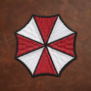 Puede incluir: Un parche bordado que presenta un diseño de paraguas octogonal con segmentos triangulares alternos en rojo y blanco. Toda la forma está delineada con un borde negro grueso, creando un patrón gráfico distintivo con un acabado de hilo texturizado.