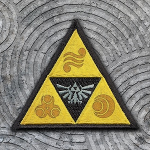 May include: Embroidered patch featuring a yellow triangle with a black border. The triangle is divided into three sections, each with a different symbol. The center section is black with a silver emblem. The background is a textured gray surface.