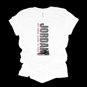 Puede incluir: Camiseta blanca con un gr&aacute;fico rojo y negro de una zapatilla de baloncesto y el texto "JORDAN MY SHOE GAME IS FIRE!"